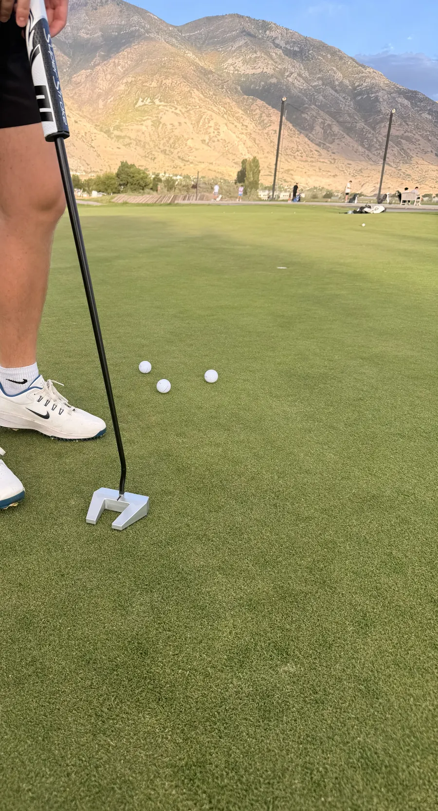 Putter in use on a practice green, SuperStroke grip visible, golf balls nearby