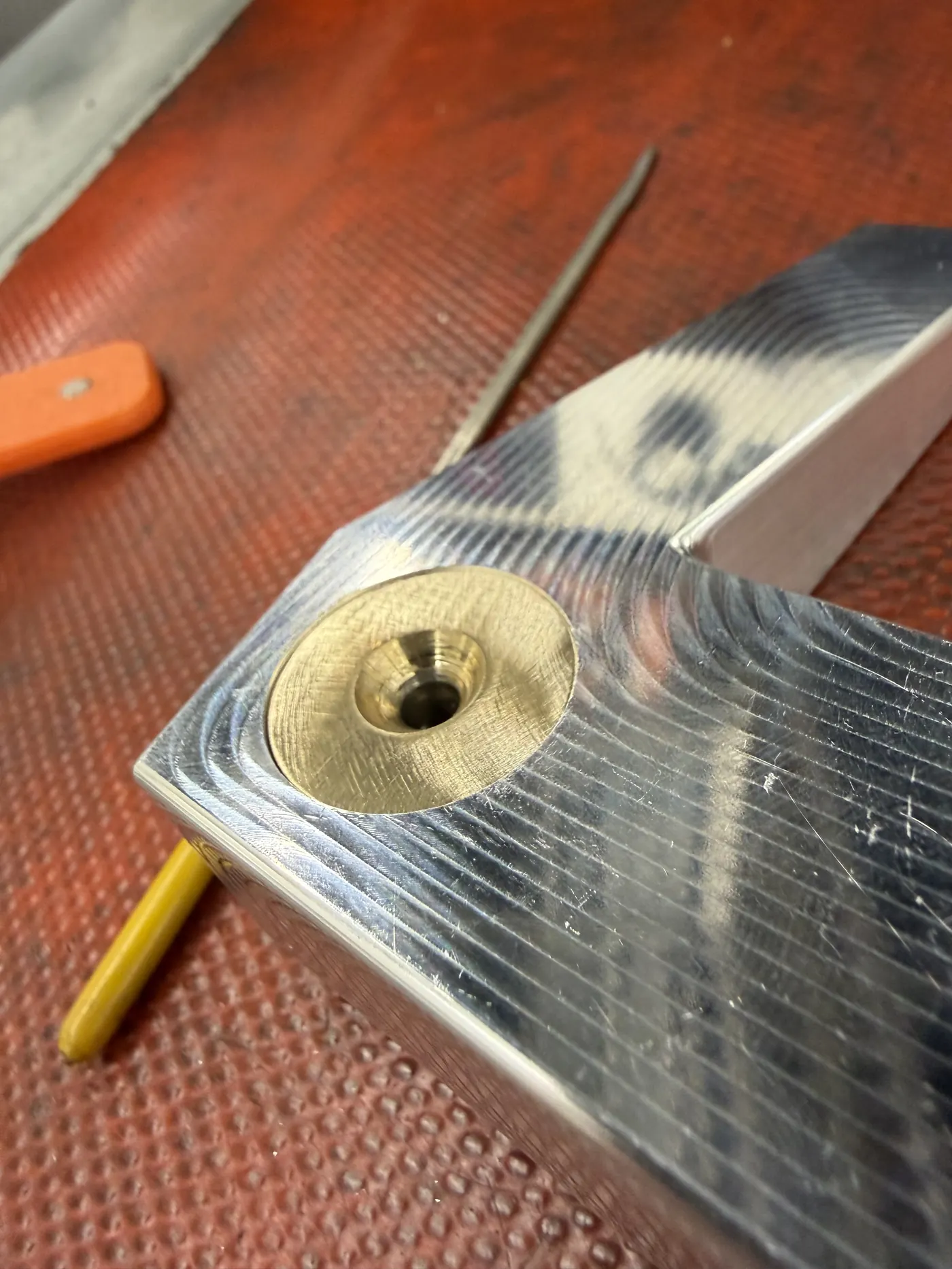 Close-up of a brass weight seated in the machined pocket, shown next to a pencil for scale